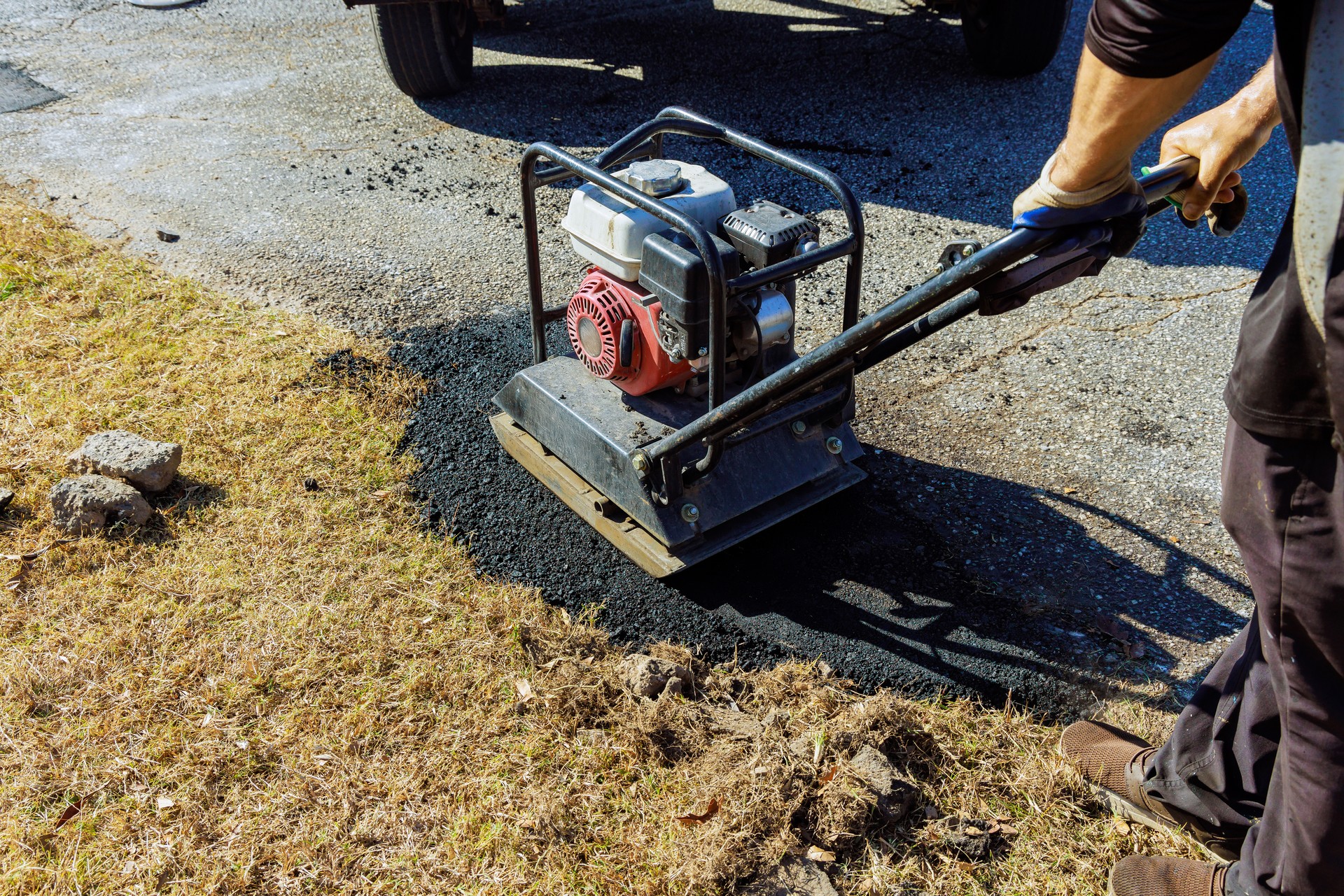 Tamping asphalt manually using tamping machine at a parking lot repair site